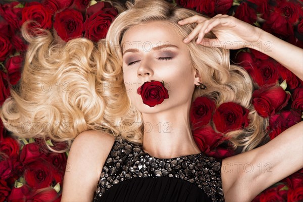 Beautiful blond girl lying on a background of roses. Curls