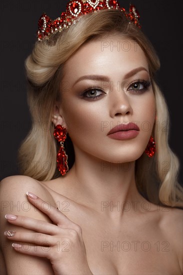 Beautiful blond girl with a golden crown and earrings and professional evening make-up. Beauty face. Picture taken in the studio