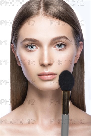 Beautiful young girl with a light natural make-up and beauty tools in hand. Picture taken in the studio on a white background