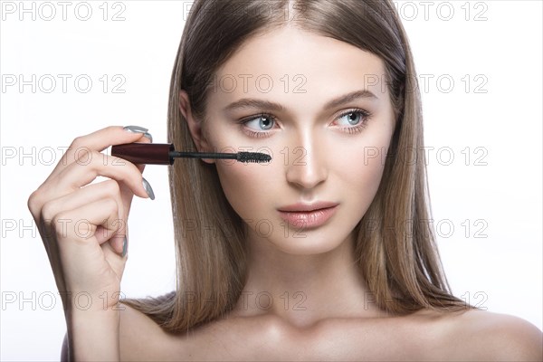 Beautiful young girl with a light natural make-up and beauty tools in hand. Picture taken in the studio on a white background