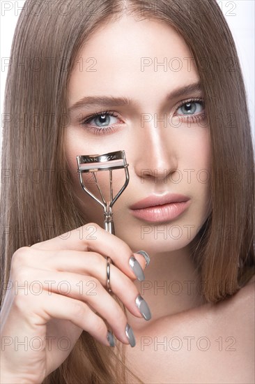 Beautiful young girl with a light natural make-up and beauty tools in hand. Picture taken in the studio on a white background