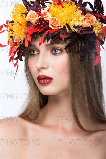 Beautiful girl with bright autumn wreath of leaves and flowers. Beauty face. Picture taken in the studio on a white background