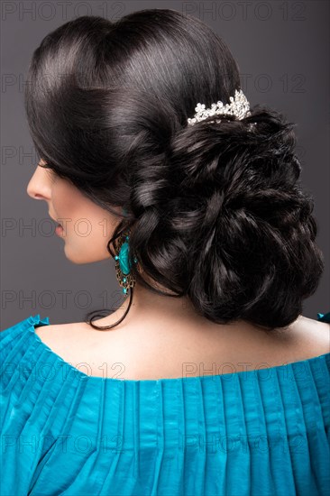 Beautiful girl in a blue dress with evening make-up and hairstyle. Beauty face. Picture taken in the studio on a black background. Hairstyle back view
