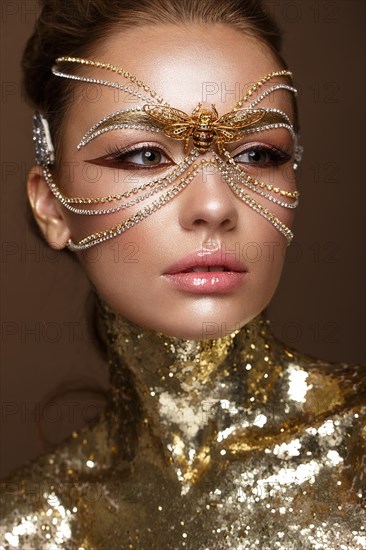 Beautiful girl in a golden mask and bright evening make-up. Beauty face. Photo taken in studio