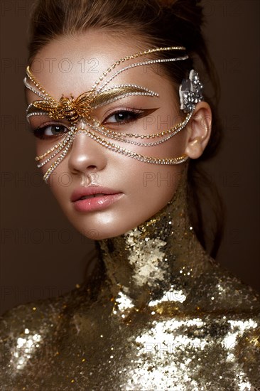 Beautiful girl in a golden mask and bright evening make-up. Beauty face. Photo taken in studio