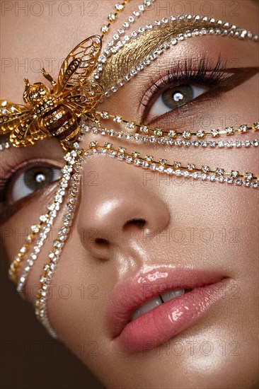 Beautiful girl in a golden mask and bright evening make-up. Beauty face. Photo taken in studio