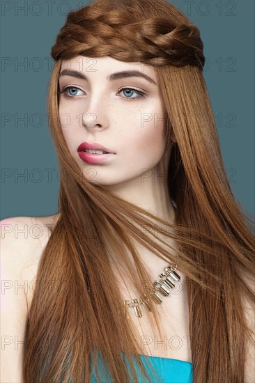 Beautiful red-haired girl with a pigtail hair and unusual lips. Portrait shot in the studio on a blue background