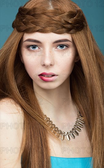 Beautiful red-haired girl with a pigtail hair and unusual lips. Portrait shot in the studio on a blue background