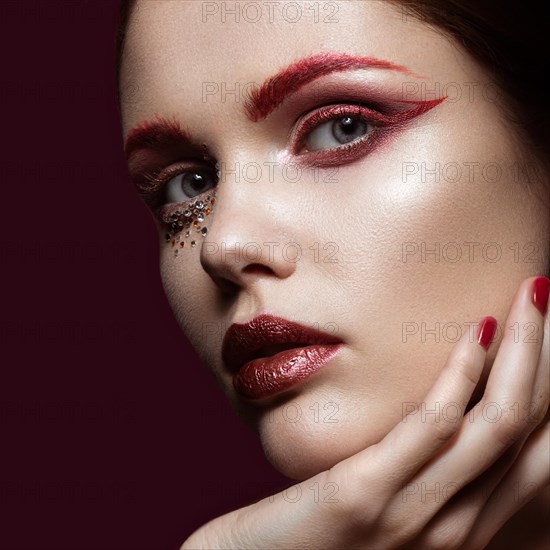Beautiful girl with a bright red fashion makeup and crystals on the face. Close-up portrait. Beauty face. Picture taken in the studio