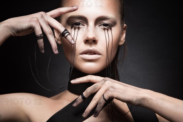 Beautiful girl with creative make-up in Gothic style and the threads of eyes. Art beauty face. Picture taken in the studio on a black background