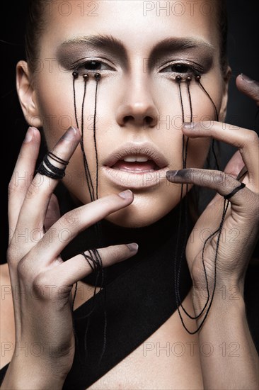 Beautiful girl with creative make-up in Gothic style and the threads of eyes. Art beauty face. Picture taken in the studio on a black background