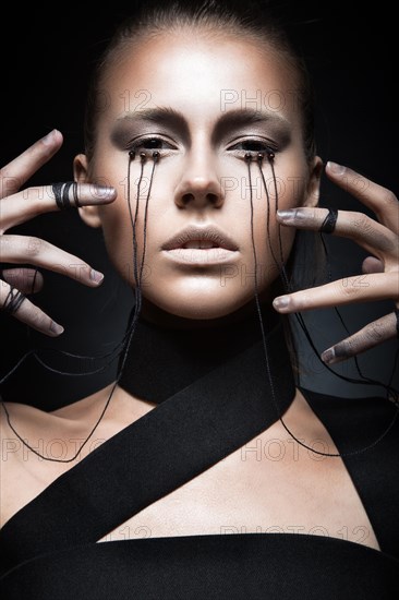 Beautiful girl with creative make-up in Gothic style and the threads of eyes. Art beauty face. Picture taken in the studio on a black background