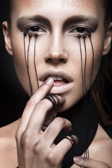 Beautiful girl with creative make-up in Gothic style and the threads of eyes. Art beauty face. Picture taken in the studio on a black background