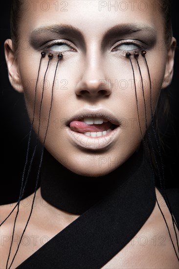 Beautiful girl with creative make-up in Gothic style and the threads of eyes. Art beauty face. Picture taken in the studio on a black background