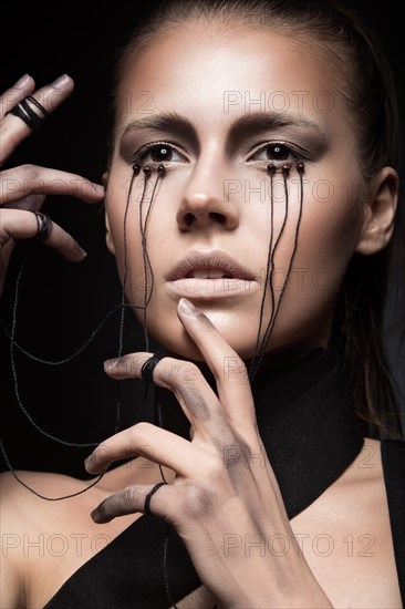 Beautiful girl with creative make-up in Gothic style and the threads of eyes. Art beauty face. Picture taken in the studio on a black background