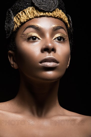 African girl with bright makeup and creative gold accessories on the head. Beauty face. Picture taken in the studio on a black background