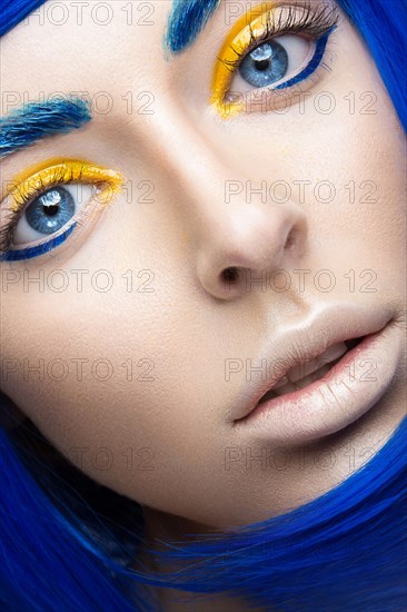 Beautiful girl in a bright blue wig in the style of cosplay and creative makeup. Beauty face. Art image. Picture taken in the studio on a yellow background