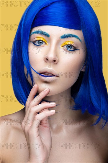 Beautiful girl in a bright blue wig in the style of cosplay and creative makeup. Beauty face. Art image. Picture taken in the studio on a yellow background
