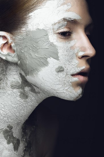 Beautiful girl with mud on his face. Cosmetic mask. Beauty face. Picture taken in the studio on a black background