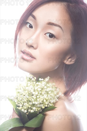 Fashion beautiful girl oriental type with delicate natural make-up and flowers. Beauty face. Picture taken in the studio on a white background