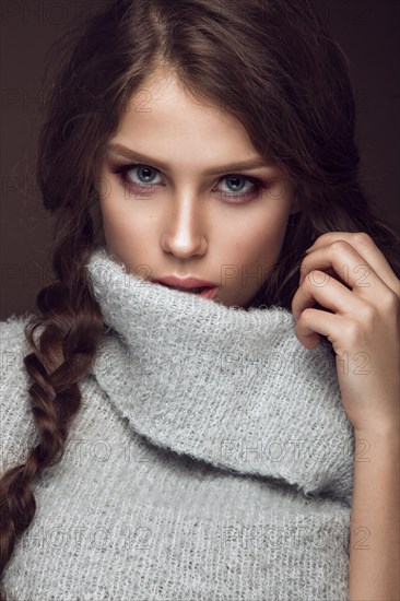 Beautiful young girl with gentle make-up in warm sweater and long straight hair. Beauty face. Studio portrait