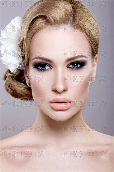 Portrait of a beautiful blonde woman in the image of the bride with flowers in her hair. Picture taken in the studio on a blue background