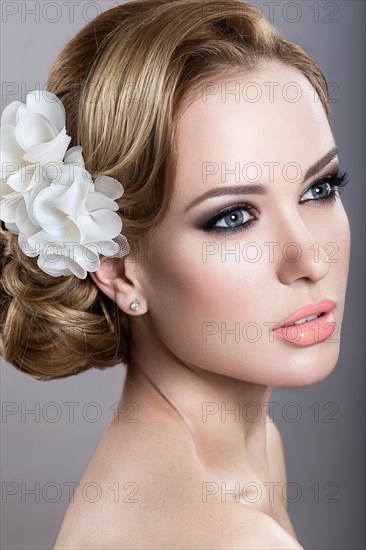 Portrait of a beautiful blonde woman in the image of the bride with flowers in her hair. Picture taken in the studio on a blue background