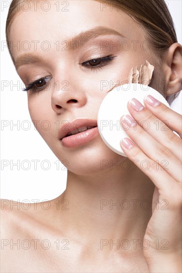 Beautiful young girl with sponge for application make-up and French manicure. Beauty face. Picture taken in the studio on a white background