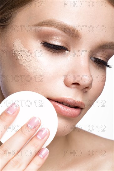 Beautiful young girl with sponge for application make-up and French manicure. Beauty face. Picture taken in the studio on a white background