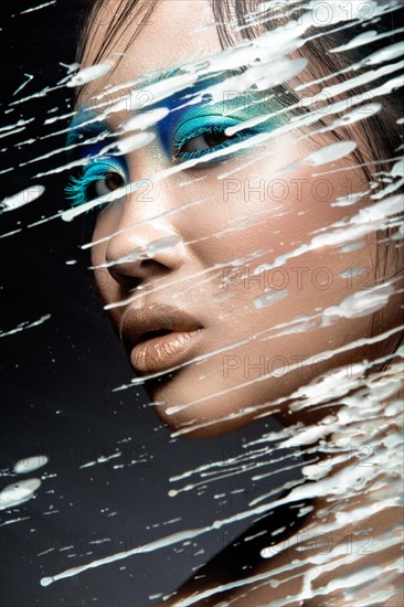 Beautiful Asian girl with bright blue make-up behind glass with drops of wax. Beauty face. Picture taken in the studio on a black background