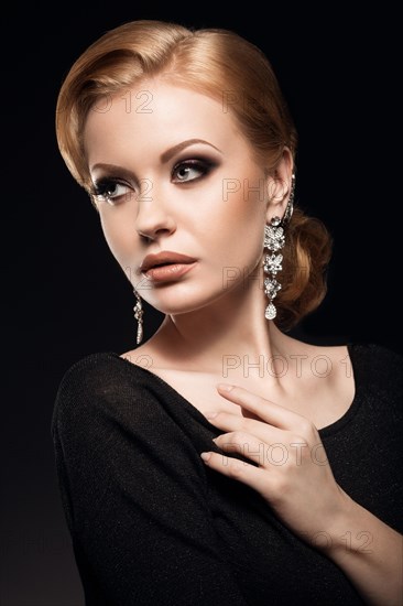 Beautiful red-haired girl in a black dress with a smooth evening haircut in the form of waves and bright makeup. Beauty face. Picture taken in the studio on a black background