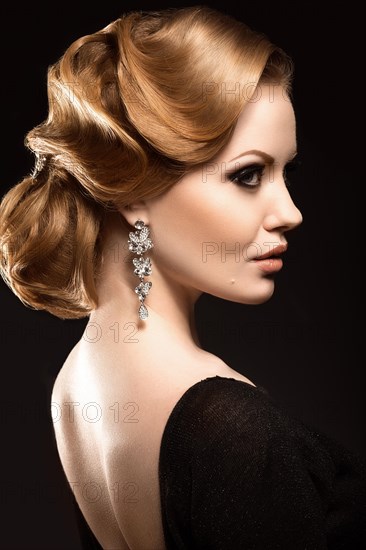 Beautiful red-haired girl in a black dress with a smooth evening haircut in the form of waves and bright makeup. Beauty face. Picture taken in the studio on a black background