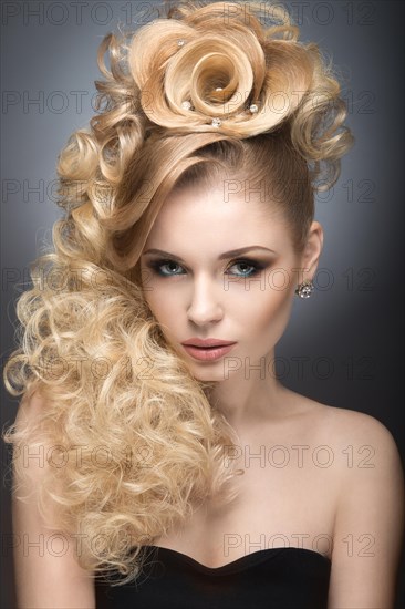 Beautiful blonde girl in evening dress with an unusual hairstyle in the form of roses and bright makeup. Beauty face. Picture taken in the studio on a gray background