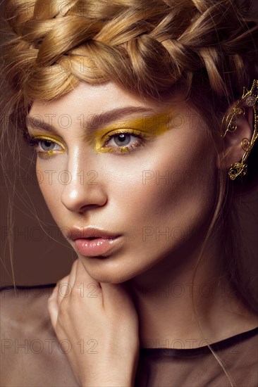 Beautiful girl in a gold dress with creative makeup and braids on her head. The beauty of the face. Photos shot in the studio