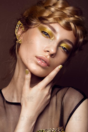 Beautiful girl in a gold dress with creative makeup and braids on her head. The beauty of the face. Photos shot in the studio