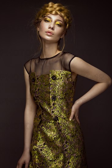 Beautiful girl in a gold dress with creative makeup and braids on her head. The beauty of the face. Photos shot in the studio