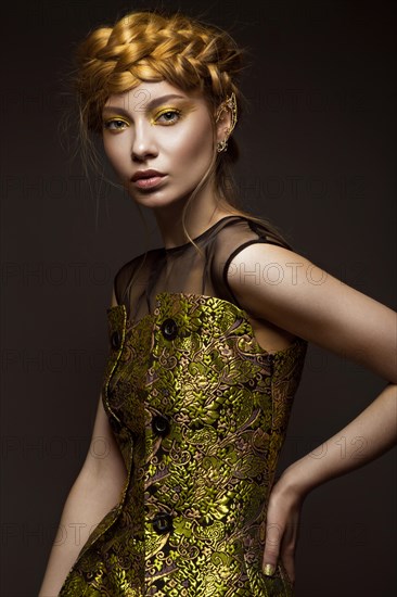 Beautiful girl in a gold dress with creative makeup and braids on her head. The beauty of the face. Photos shot in the studio