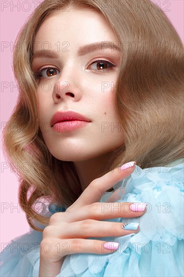 Beautiful girl with light make-up and gentle manicure in blue clothes. Beauty face. Design nails. Photo taken in studio on pink background