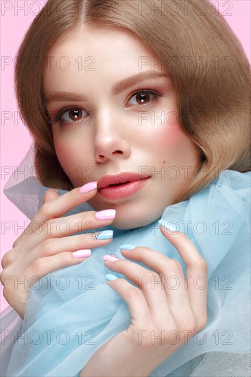 Beautiful girl with light make-up and gentle manicure in blue clothes. Beauty face. Design nails. Photo taken in studio on pink background