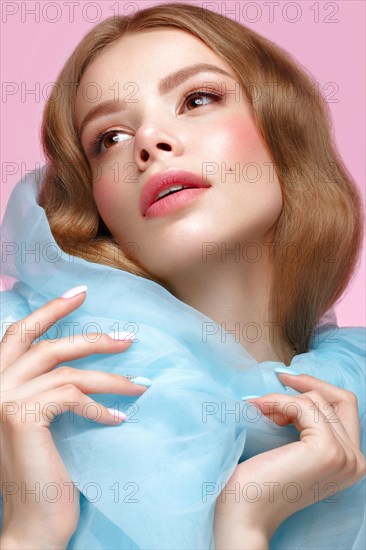 Beautiful girl with light make-up and gentle manicure in blue clothes. Beauty face. Design nails. Photo taken in studio on pink background