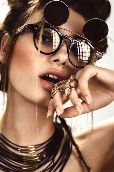 Beautiful fashion woman with creative make-up and hairstyle wearing glasses and jewelry. The beauty of the face. Photos shot in the studio