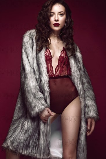 Beautiful sexy long-haired brunette woman in red lingerie and fur coat posing in the studio. The beauty of the face and body. Photos shot in a studio
