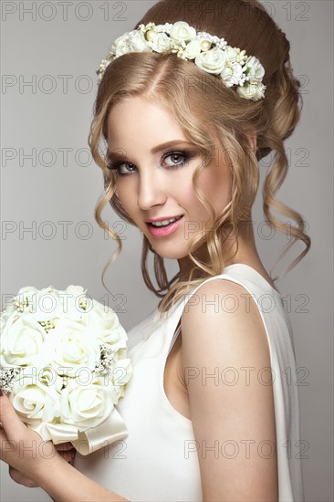Portrait of a beautiful blond girl in image of the bride with white flowers on her head. Beauty face. Photo shot in the Studio on a grey background