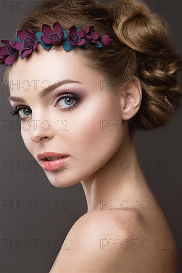 Portrait of a beautiful girl with a wreath of pink flowers on her head. Photo shot in the Studio on a grey background