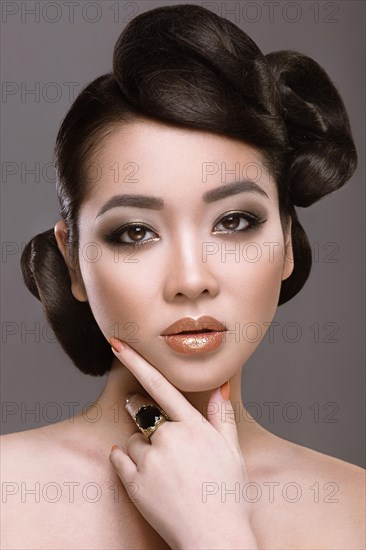 Beautiful girl with oriental type evening hair and makeup. Portrait shot in the studio on a gray background