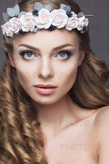 Portrait of a beautiful girl with a wreath of pink flowers on her head. Photo shot in the Studio on a grey background