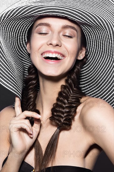 Beautiful cheerful girl in a summer beach striped hat. The beauty of the face. Photos shot in the studio