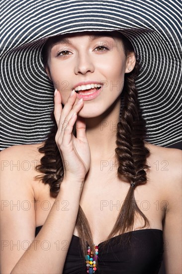 Beautiful cheerful girl in a summer beach striped hat. The beauty of the face. Photos shot in the studio