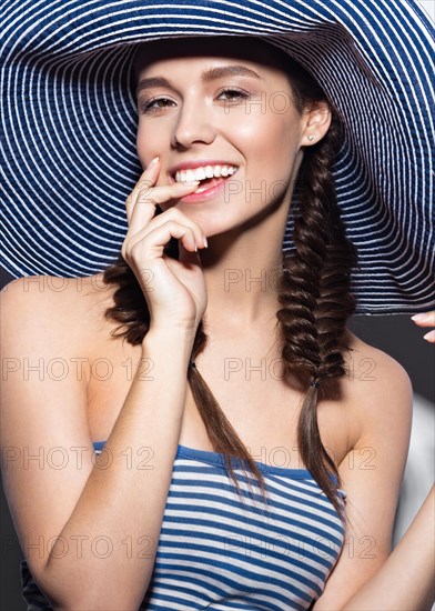 Beautiful cheerful girl in a summer beach striped hat. The beauty of the face. Photos shot in the studio
