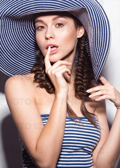 Beautiful cheerful girl in a summer beach striped hat. The beauty of the face. Photos shot in the studio